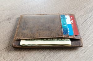 distressed brown wallet lying on a table with a blue card, red card, and money sticking out from it