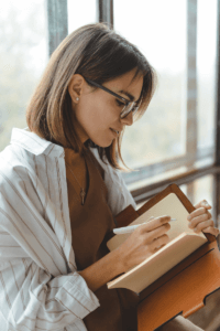 lady with brown hair and glasses writing in a journal