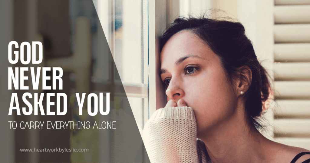 Woman in a beige sweater on leaning on a glass window with her hand to her mouth and a worried look because she's trying to carry it all